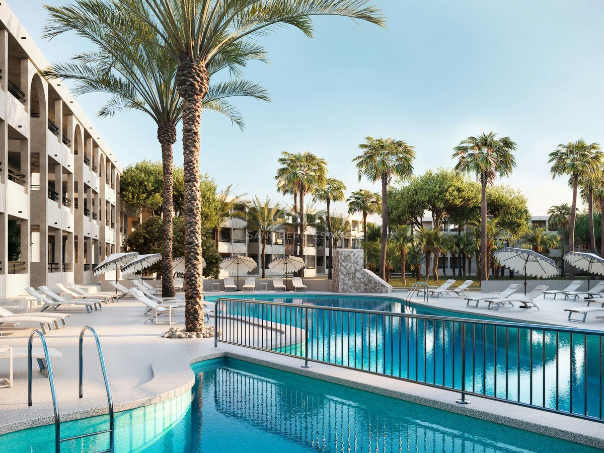Large outdoor swimming pool surrounded by white lounge chairs, palm trees, and a modern multi-story building with arches.