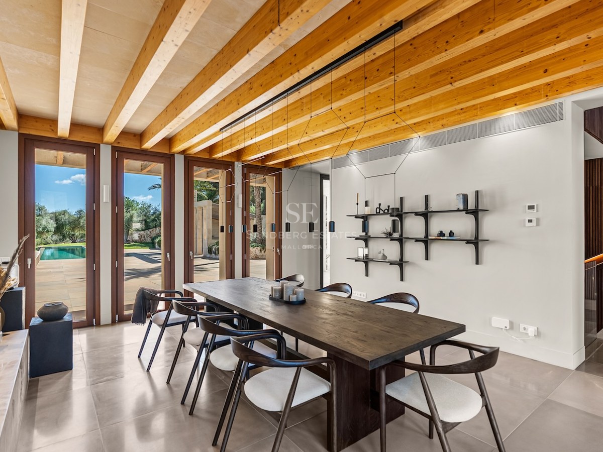 Modern dining room featuring a dark wood table, designer chairs, and a striking exposed timber beam ceiling in daylight.