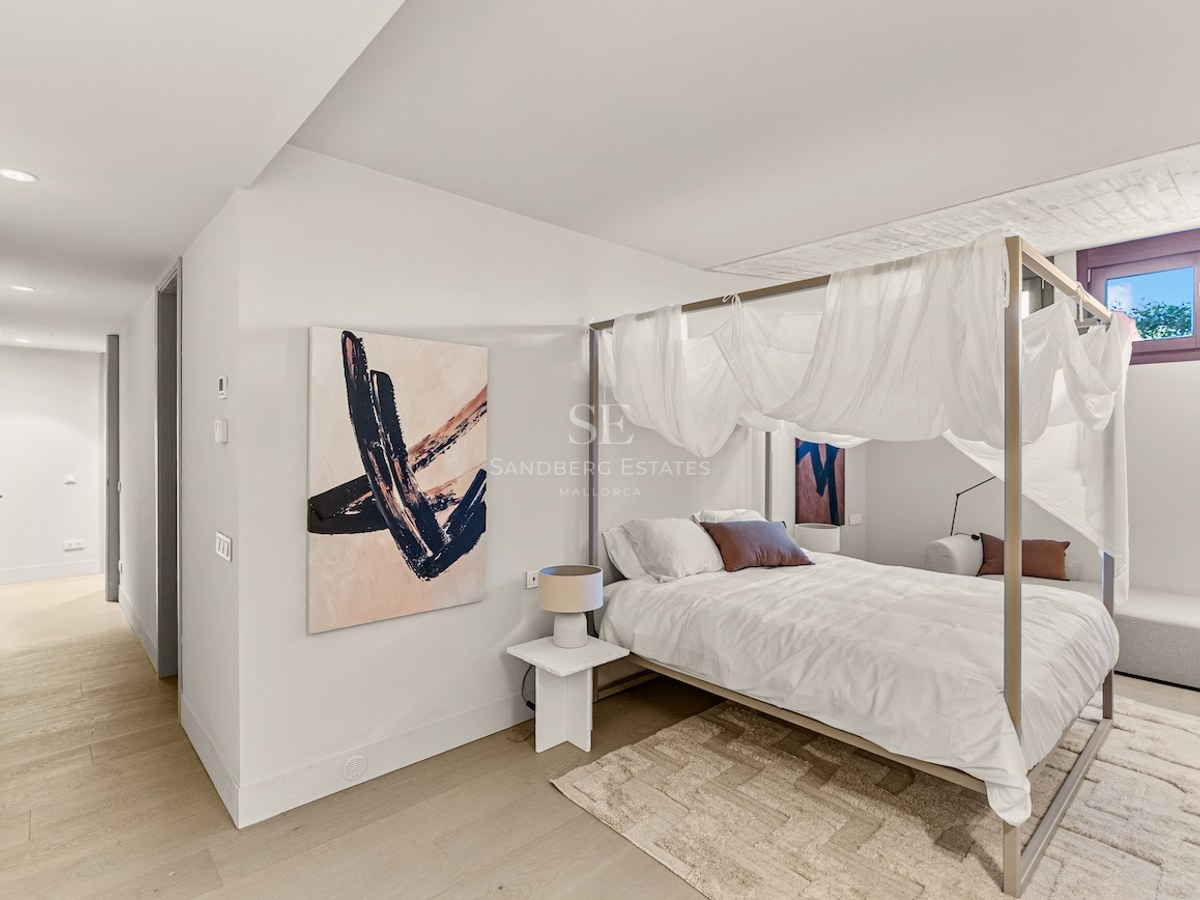 Bright bedroom featuring a four-poster canopy bed with white drapes, abstract art, and light wood flooring.
