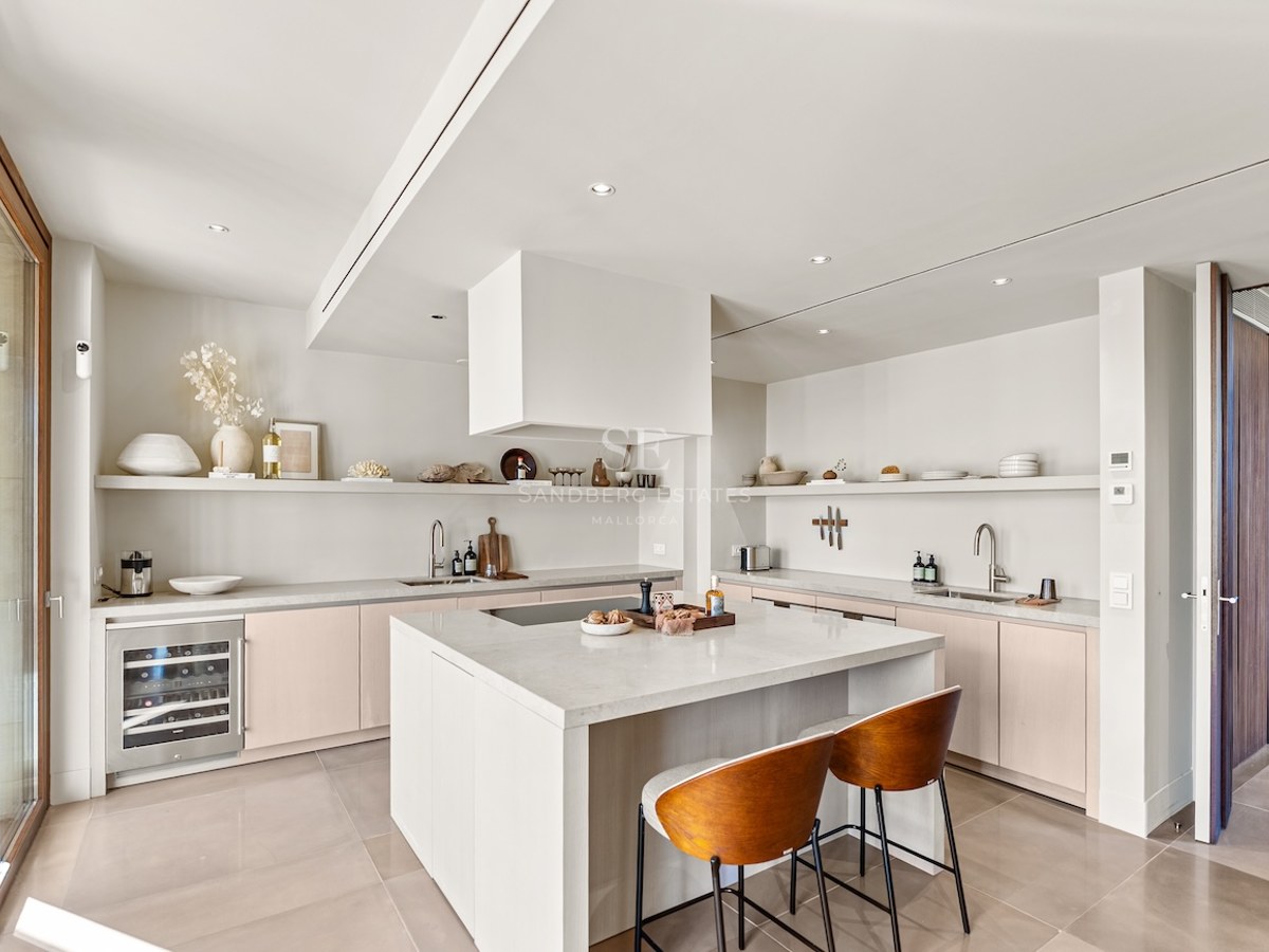 Bright modern kitchen with white island, stone countertops, wine cooler, and warm wood bar stools.