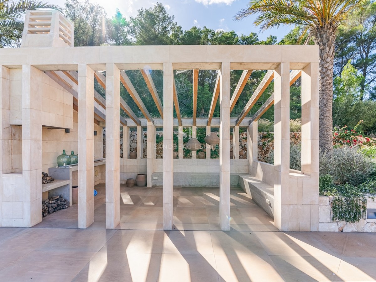 Modern stone pavilion with wooden rafters, outdoor fireplace, and built-in seating surrounded by lush greenery.