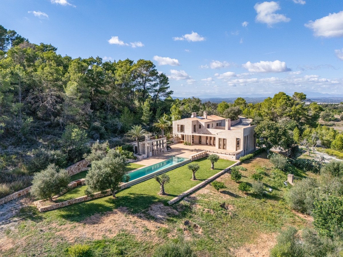 Aerial view of a luxury stone villa with a long turquoise pool surrounded by olive trees and lush forest.