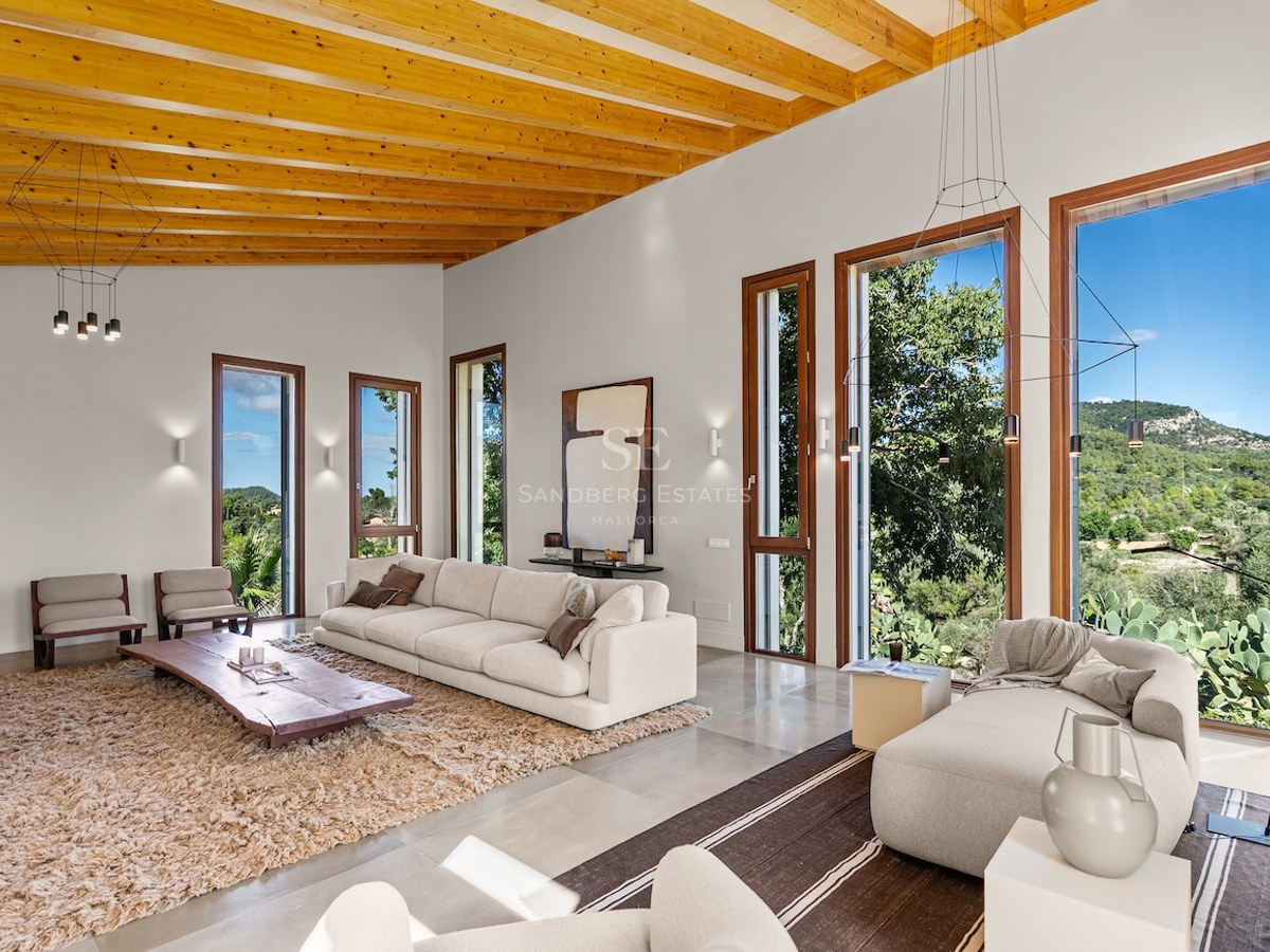 Spacious modern living room with wooden beamed ceilings, white sofas, and large windows looking out to mountains.