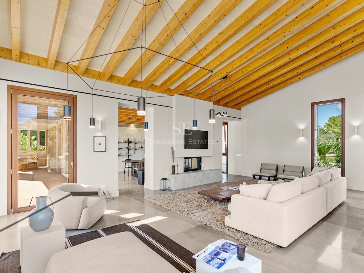 Bright living room with vaulted wood beam ceiling, cream sofas, modern fireplace, and large glass doors to a terrace.