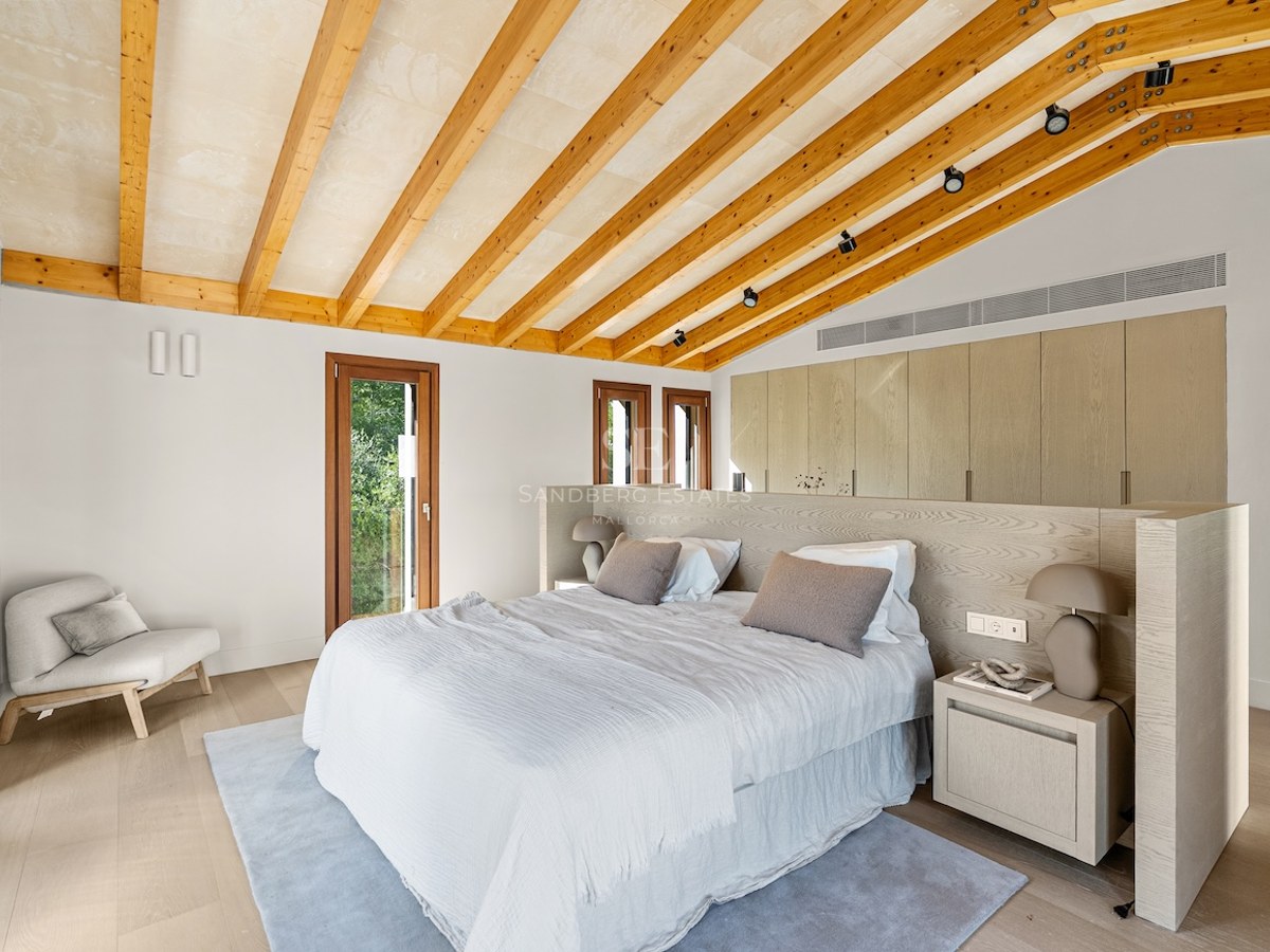 Modern master bedroom with vaulted ceiling, wooden beams, large bed, and built-in wardrobes.