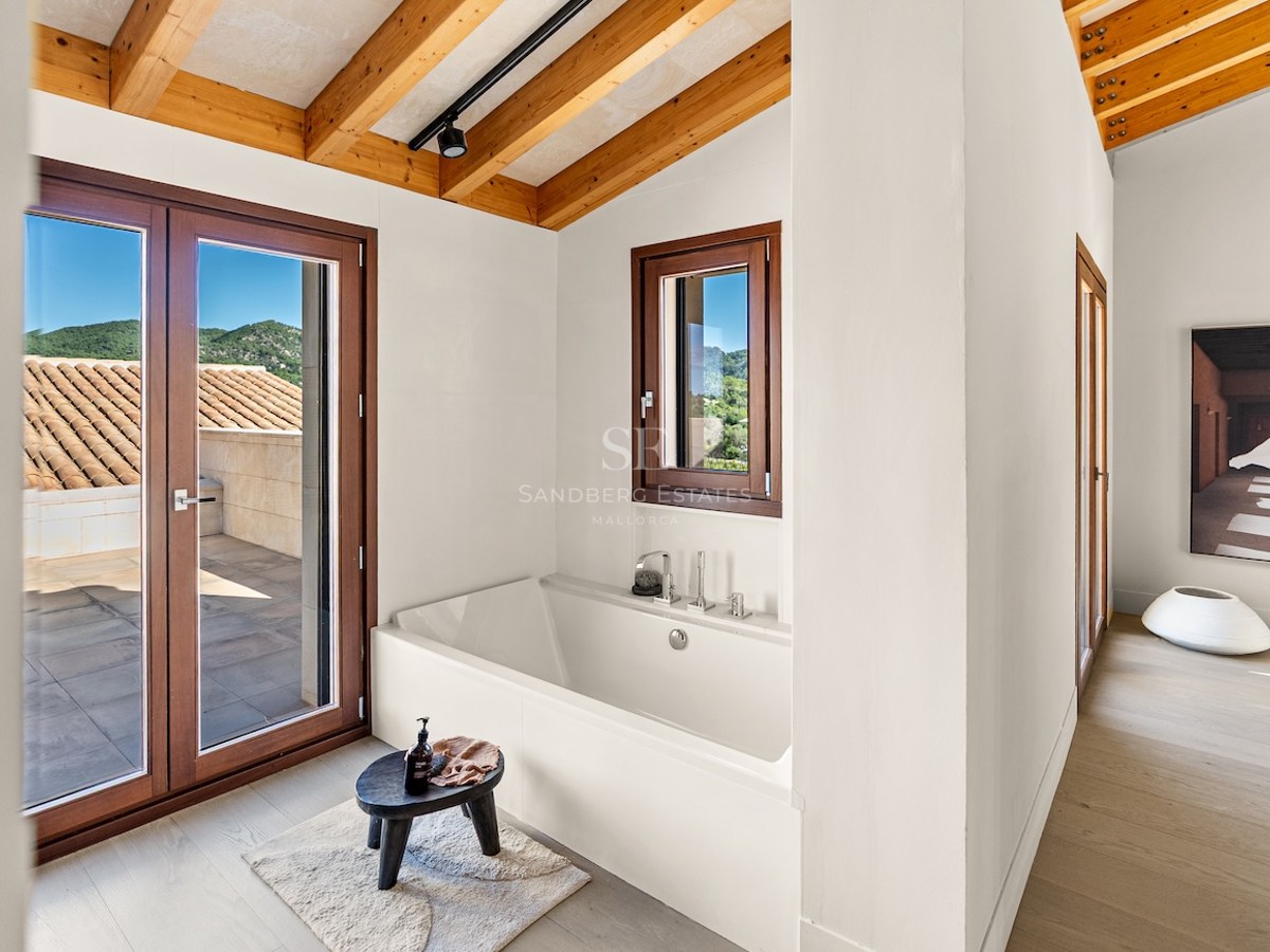 White built-in bathtub under a wooden beam ceiling with access to a terrace and mountain views.