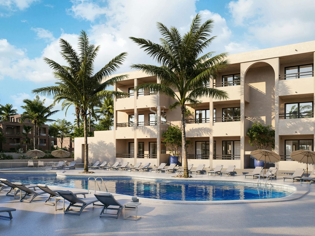 Large blue swimming pool surrounded by sun loungers and palm trees in front of a modern beige building under a clear sky.