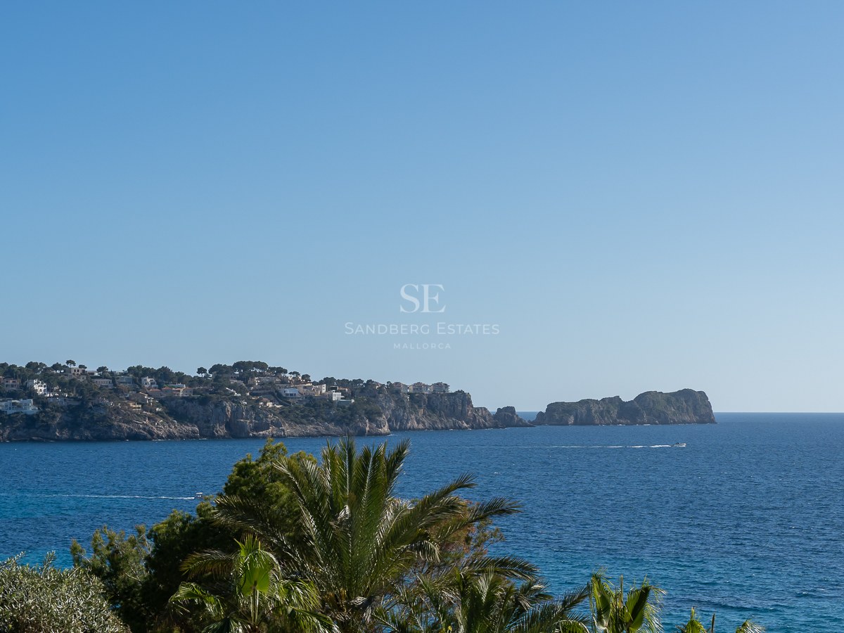 Vue panoramique de la mer Méditerranée avec des falaises, des villas de luxe et des palmiers sous un ciel bleu.