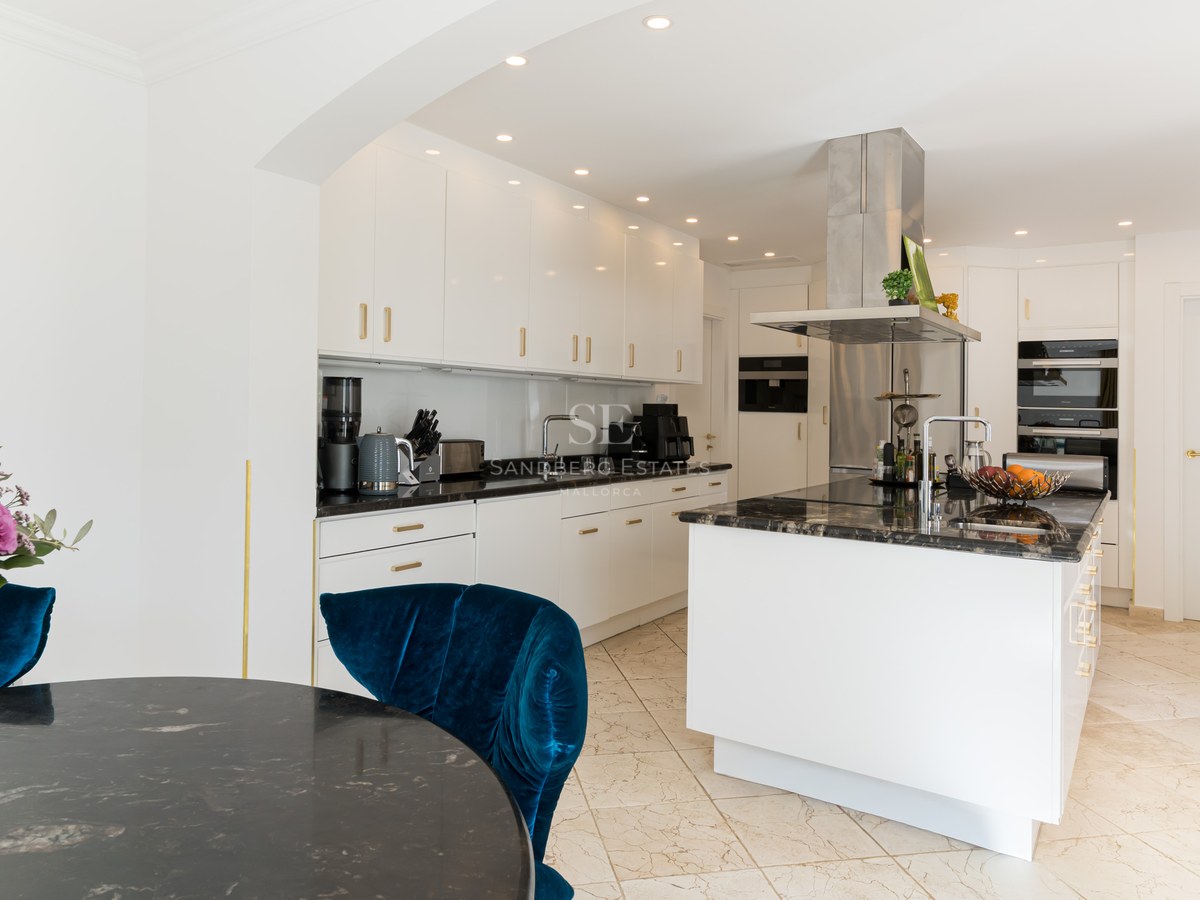 Cuisine contemporaine blanche avec plans de travail en pierre noire, îlot central et chaise en velours bleu.