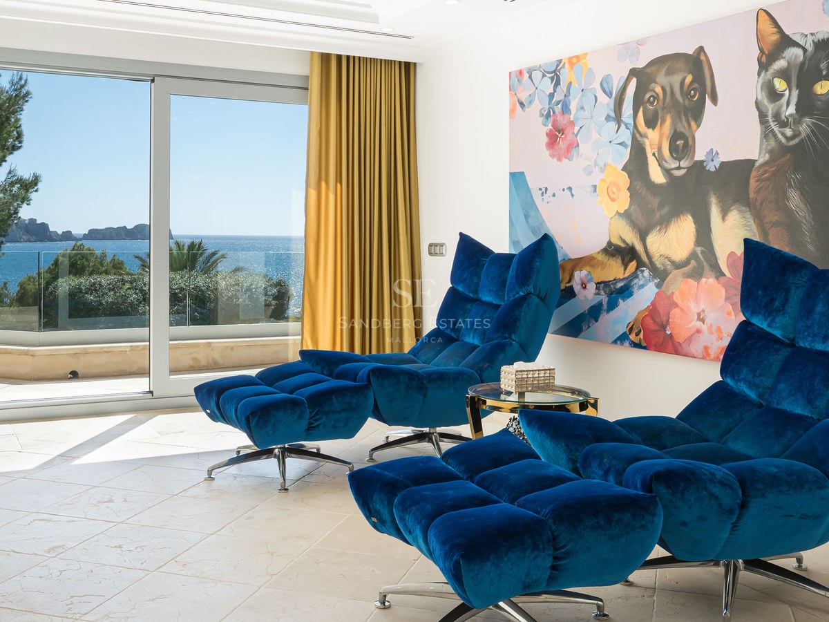 Deux fauteuils de salon en velours bleu avec repose-pieds dans une pièce lumineuse offrant une vue sur la mer.