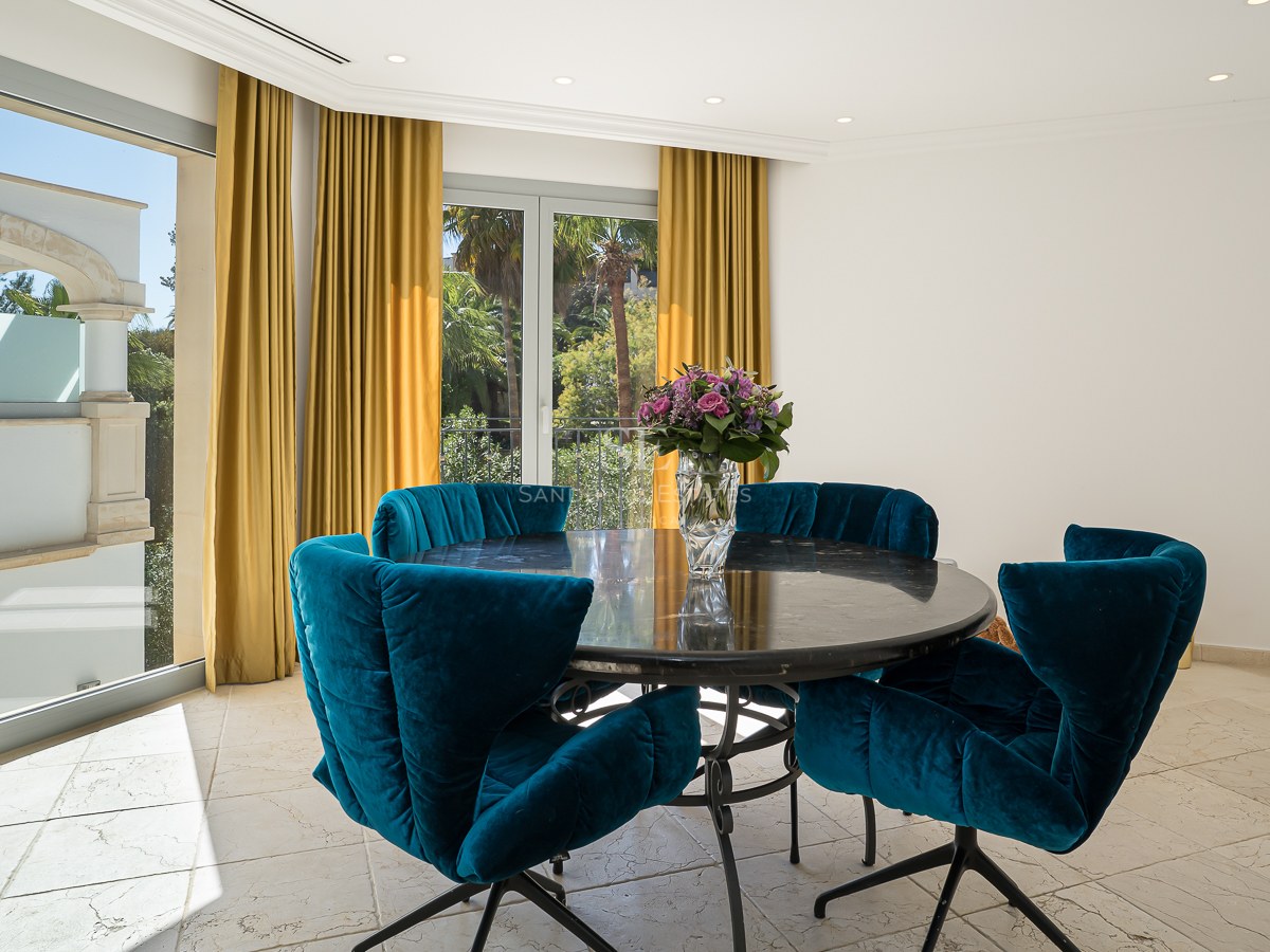 Salle à manger moderne avec table ronde en marbre, chaises en velours bleu et vue sur le jardin.
