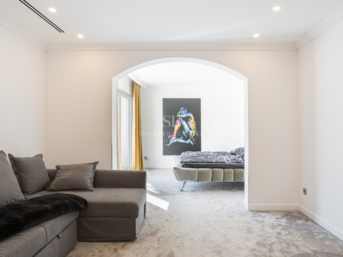 Chambre moderne vue à travers une arche avec lit gris tapissé, moquette épaisse et grande œuvre d'art murale.