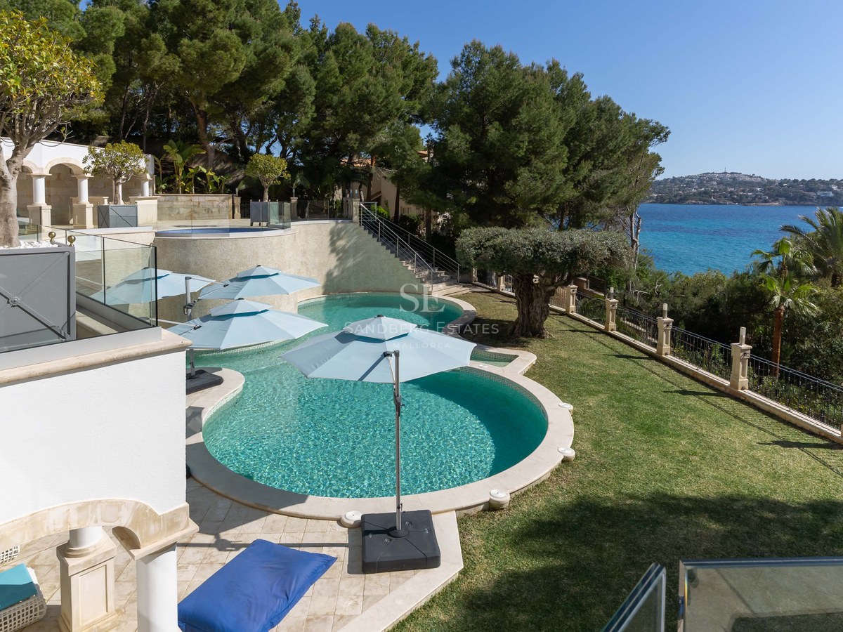 Vue en plongée d'une piscine turquoise aux formes courbes entourée d'un jardin paysager face à la mer.