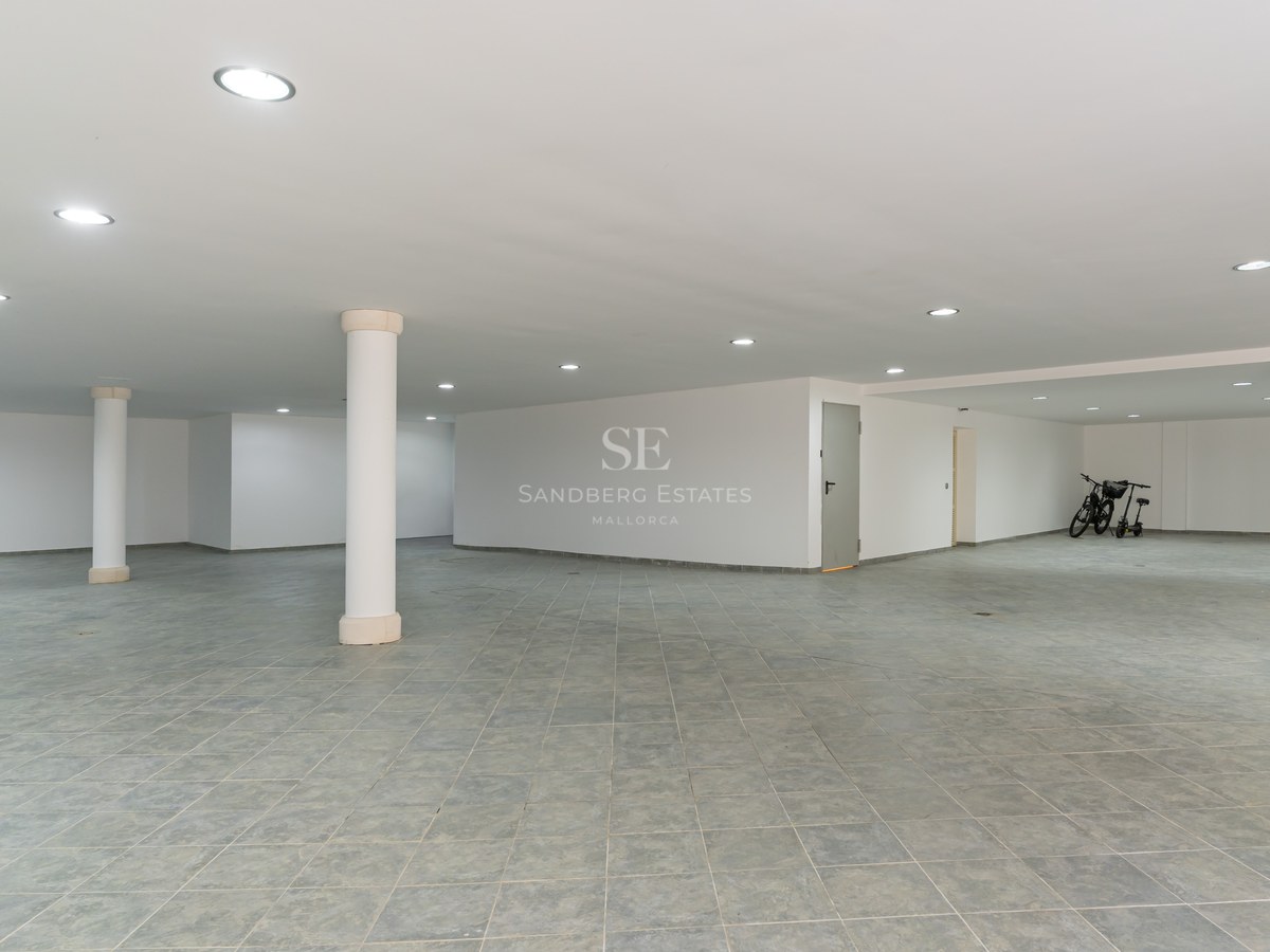 Espace de stationnement souterrain avec carrelage gris, murs blancs, éclairage LED encastré et piliers blancs.