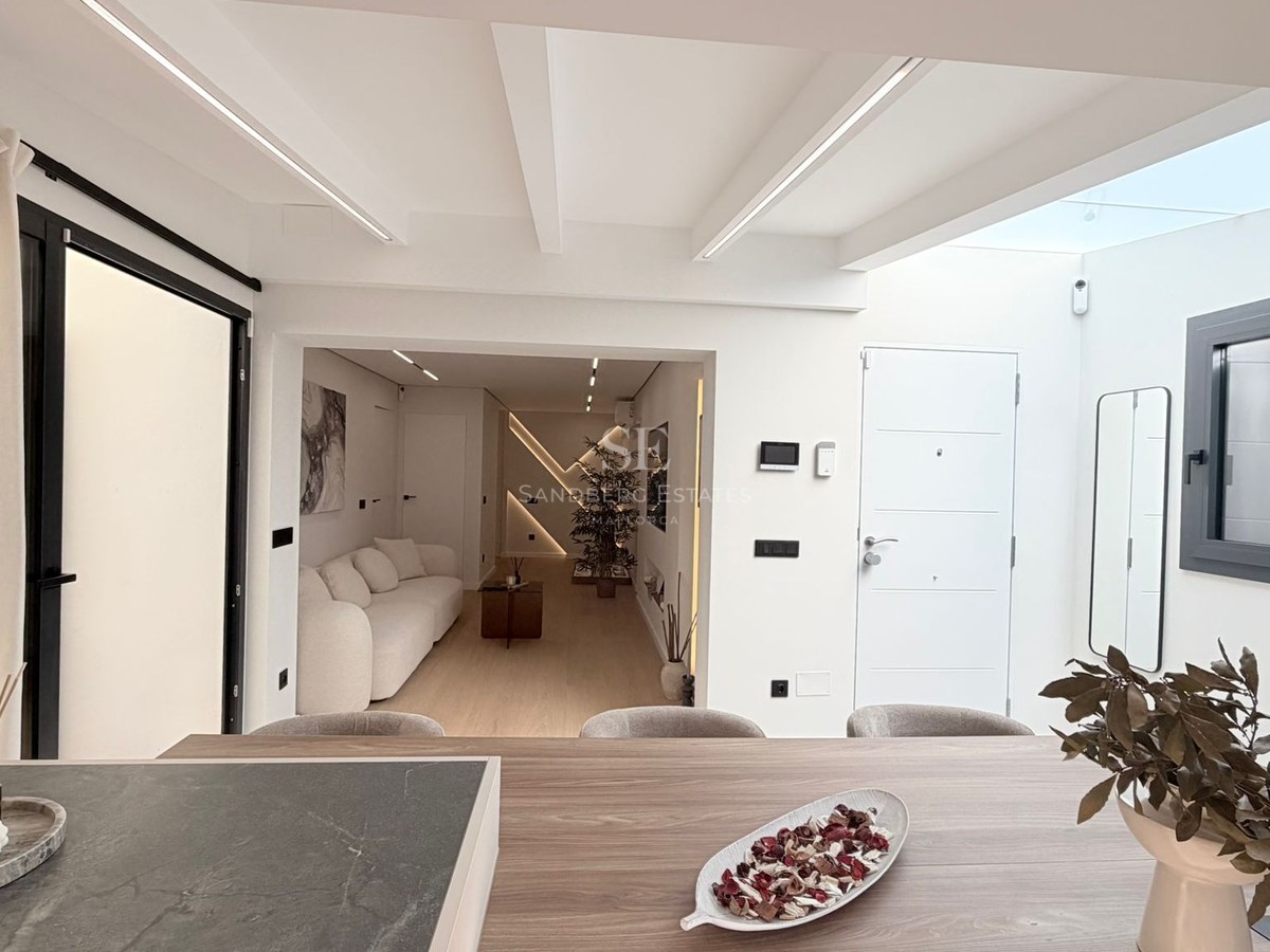 Bright modern interior featuring a white sofa, wood textures, and a skylight illuminating the living and entrance area.