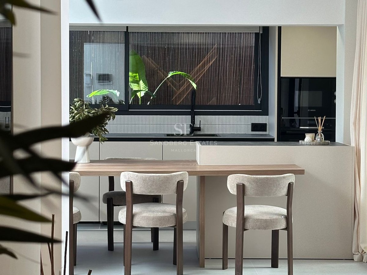 Modern kitchen featuring a light wood dining table attached to a beige island, with stylish chairs and a large window.