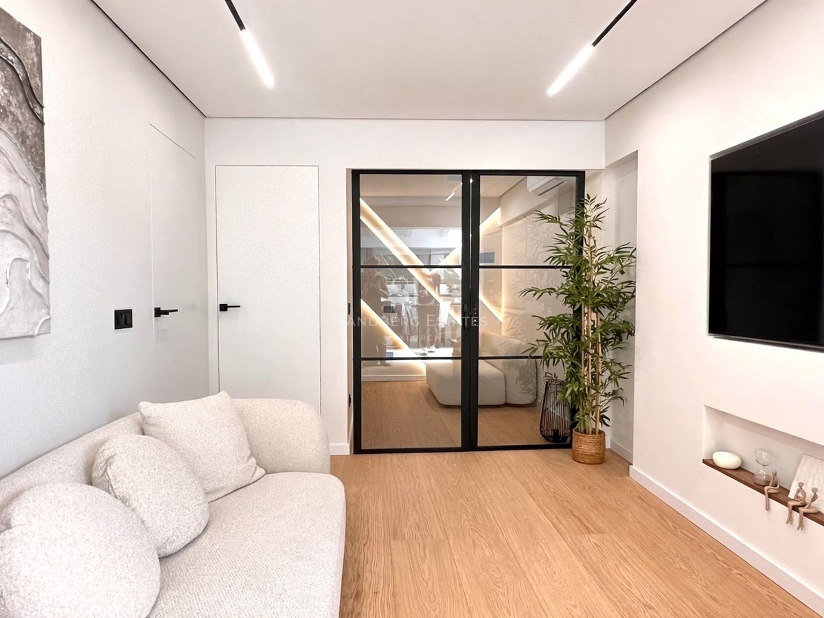Modern living room featuring a white textured sofa, light wood floors, and black-framed glass double doors.