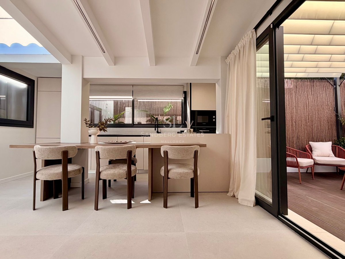 Modern dining room with wooden table and designer chairs next to a large sliding glass door opening onto a private terrace.