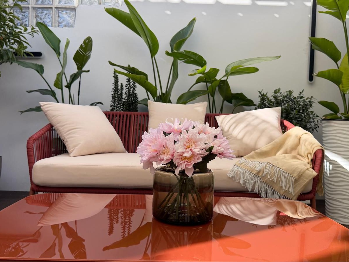 Red rope sofa with cream cushions on a terrace surrounded by tropical plants and a glossy orange coffee table.