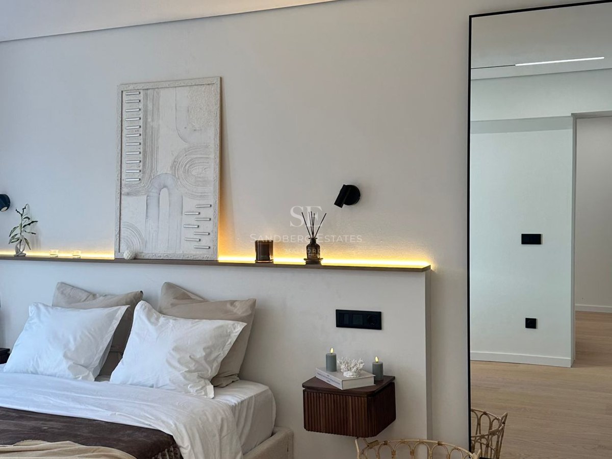 Modern bedroom featuring a white bed, LED backlighting, textured art, and a large mirror on light wood floors.
