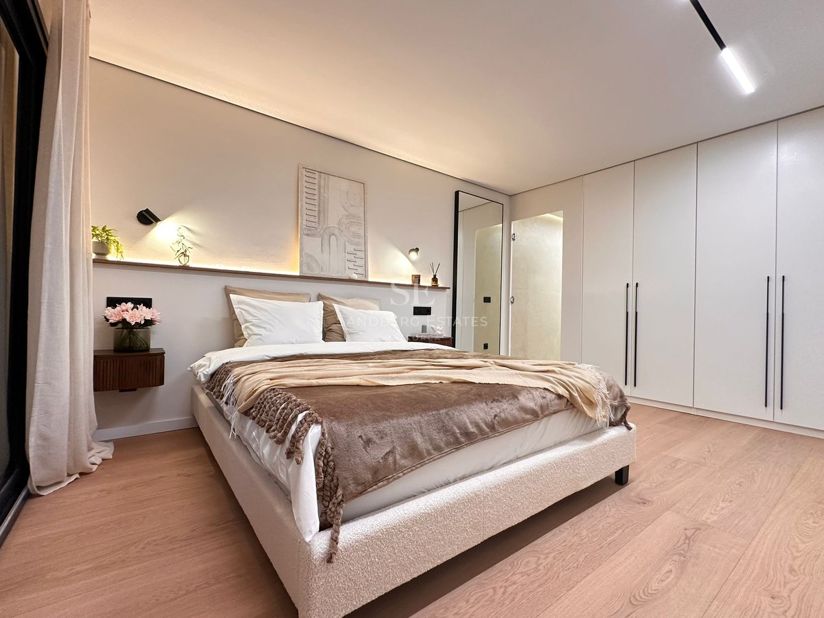 Modern master bedroom featuring a bouclé bed, ambient headboard lighting, light wood floors, and white built-in wardrobes.
