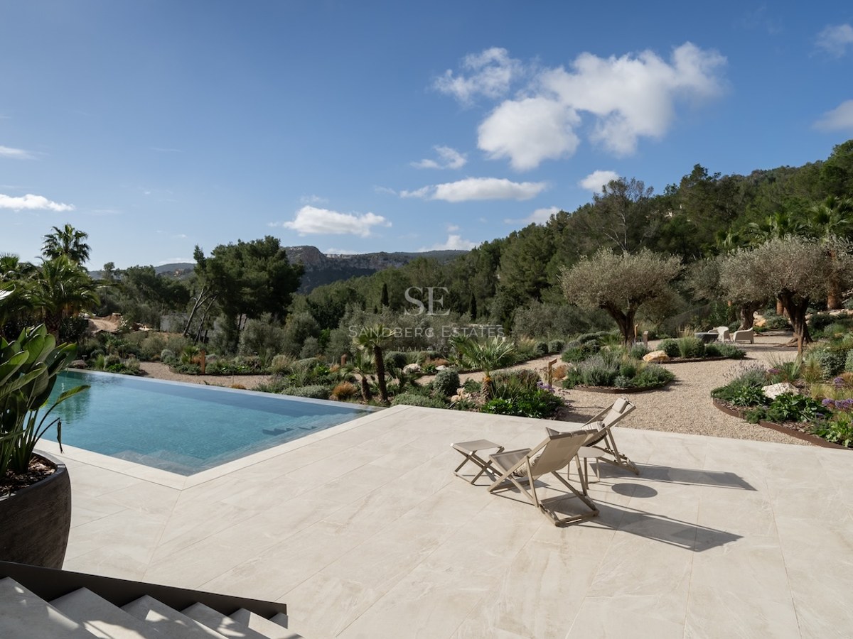 Piscina infinita y terraza de piedra con tumbonas frente a un paisaje mediterráneo de montañas y olivos.