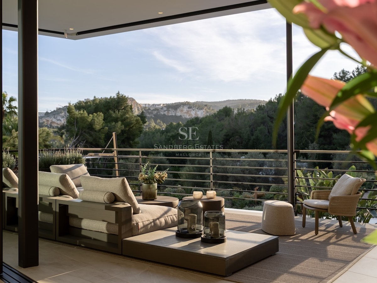 Terraza moderna con sofás modulares de madera con vistas a un valle verde y colinas arboladas bajo un cielo despejado.
