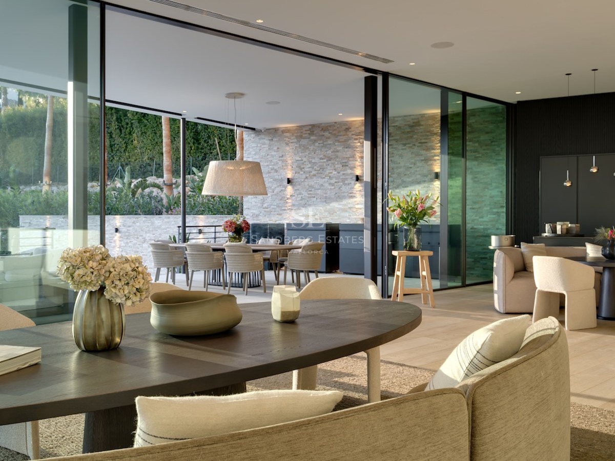 Elegante comedor con grandes ventanales de vidrio que abren a una terraza con pared de piedra y zona de estar exterior.