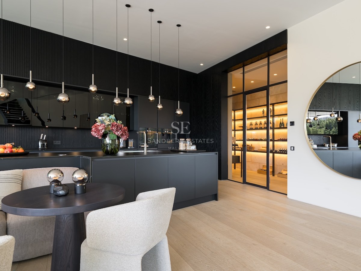 Cocina moderna en negro mate con una isla grande y una bodega de vino con paredes de cristal al fondo.