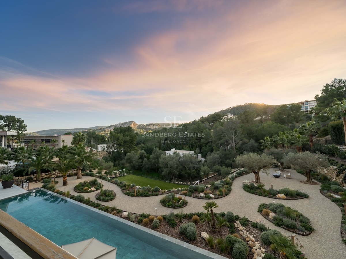 Vue en hauteur d'une piscine à débordement turquoise bordant un jardin méditerranéen paysager au crépuscule.