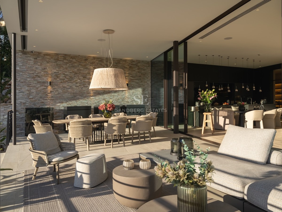 Terraza cubierta de lujo con pared de piedra natural, comedor exterior y zona lounge conectada al interior.