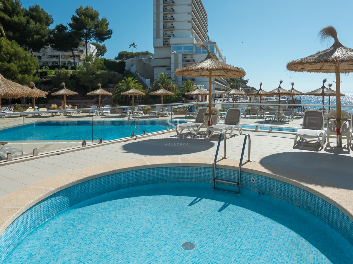 Espace piscine extérieur lumineux avec parasols en paille, transats blancs, balustrades en verre et vue sur la mer.