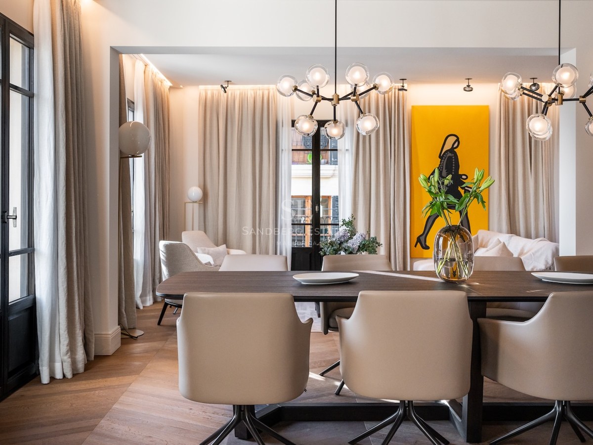 Comedor moderno con mesa de madera oscura, sillas de cuero beige y lámparas de cristal de diseño.