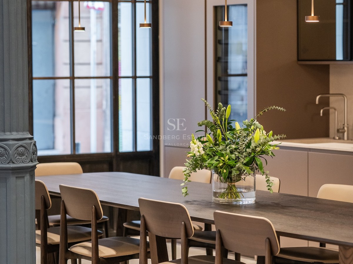 Mesa de comedor de madera oscura con sillas modernas, lámparas colgantes minimalistas y una columna decorativa.