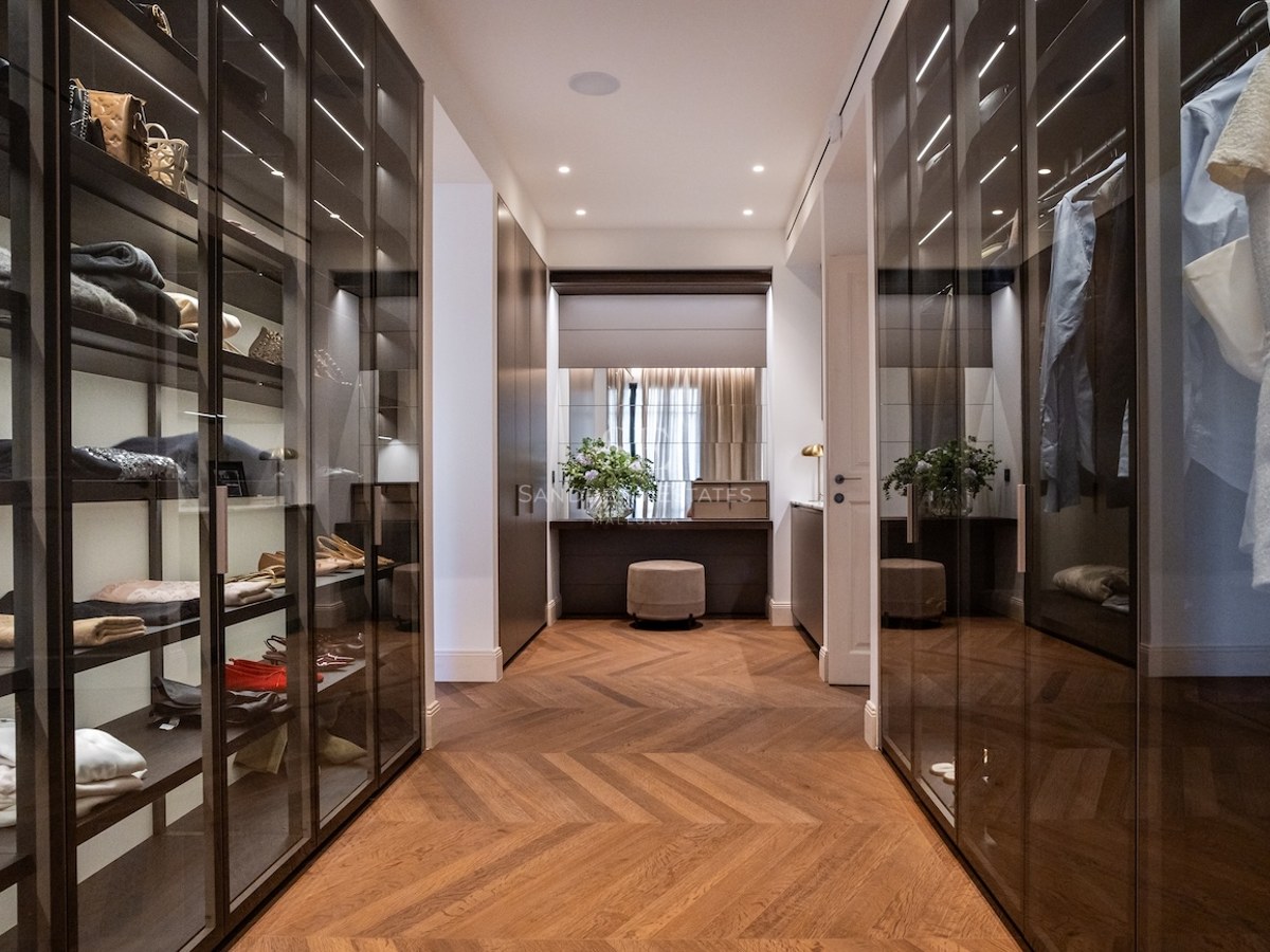 Elegante vestidor con armarios de cristal, suelos de madera en espiga y un tocador al fondo.