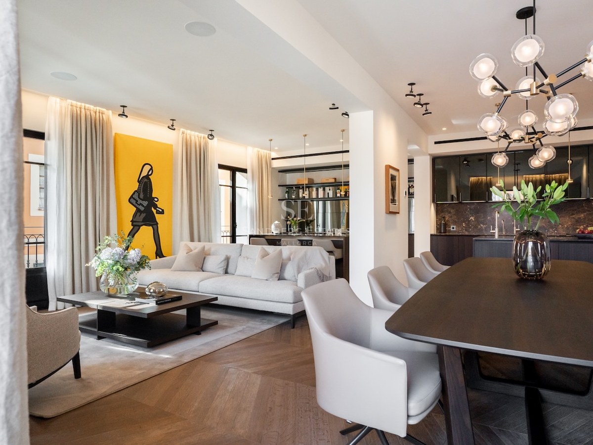 Salón de planta abierta con sofá gris, arte amarillo en la pared y zona de comedor con lámpara de diseño.