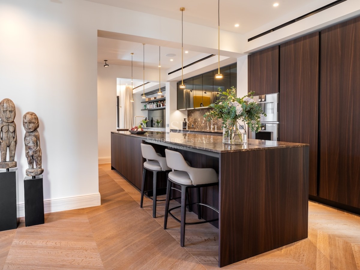 Cocina contemporánea con isla de madera oscura, encimera de mármol, taburetes de cuero y suelo de madera en espiga.