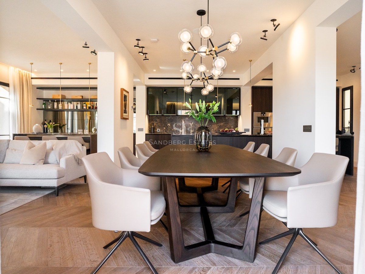 Comedor moderno con mesa de madera oscura, sillas blancas y lámpara de esferas en una casa de lujo.
