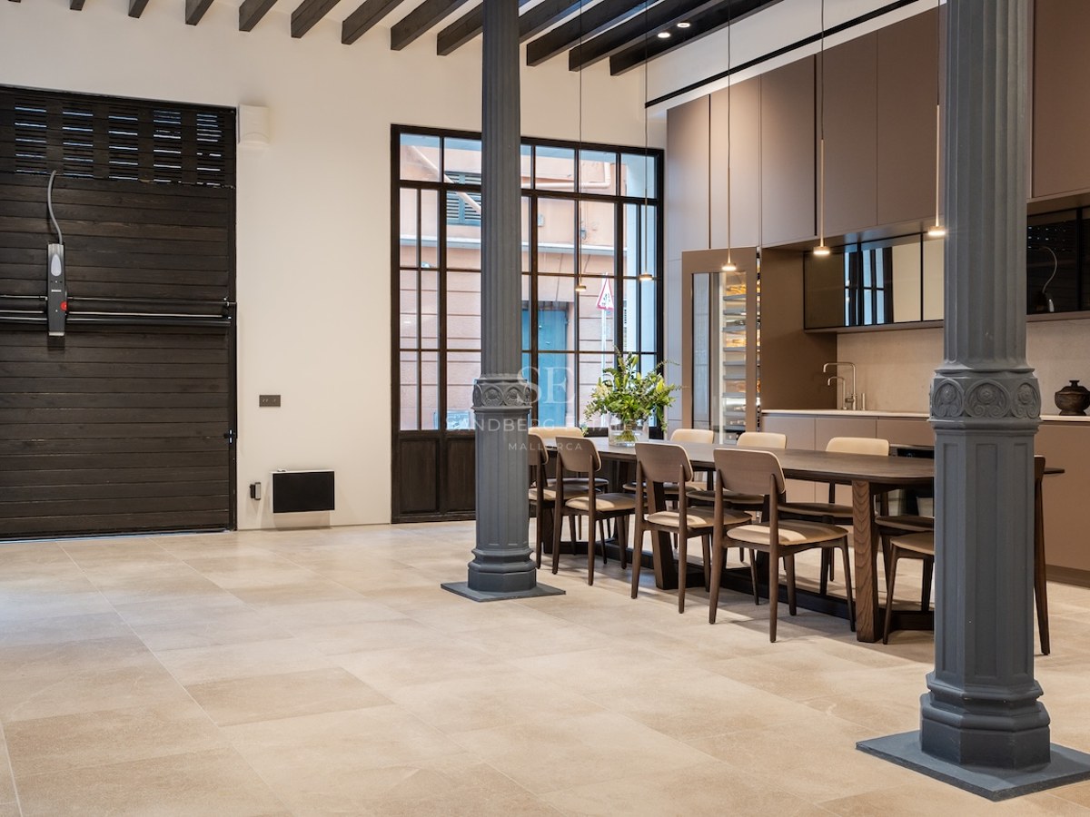 Comedor industrial con columnas estriadas, mesa de madera larga y vigas vistas en un espacio abierto.