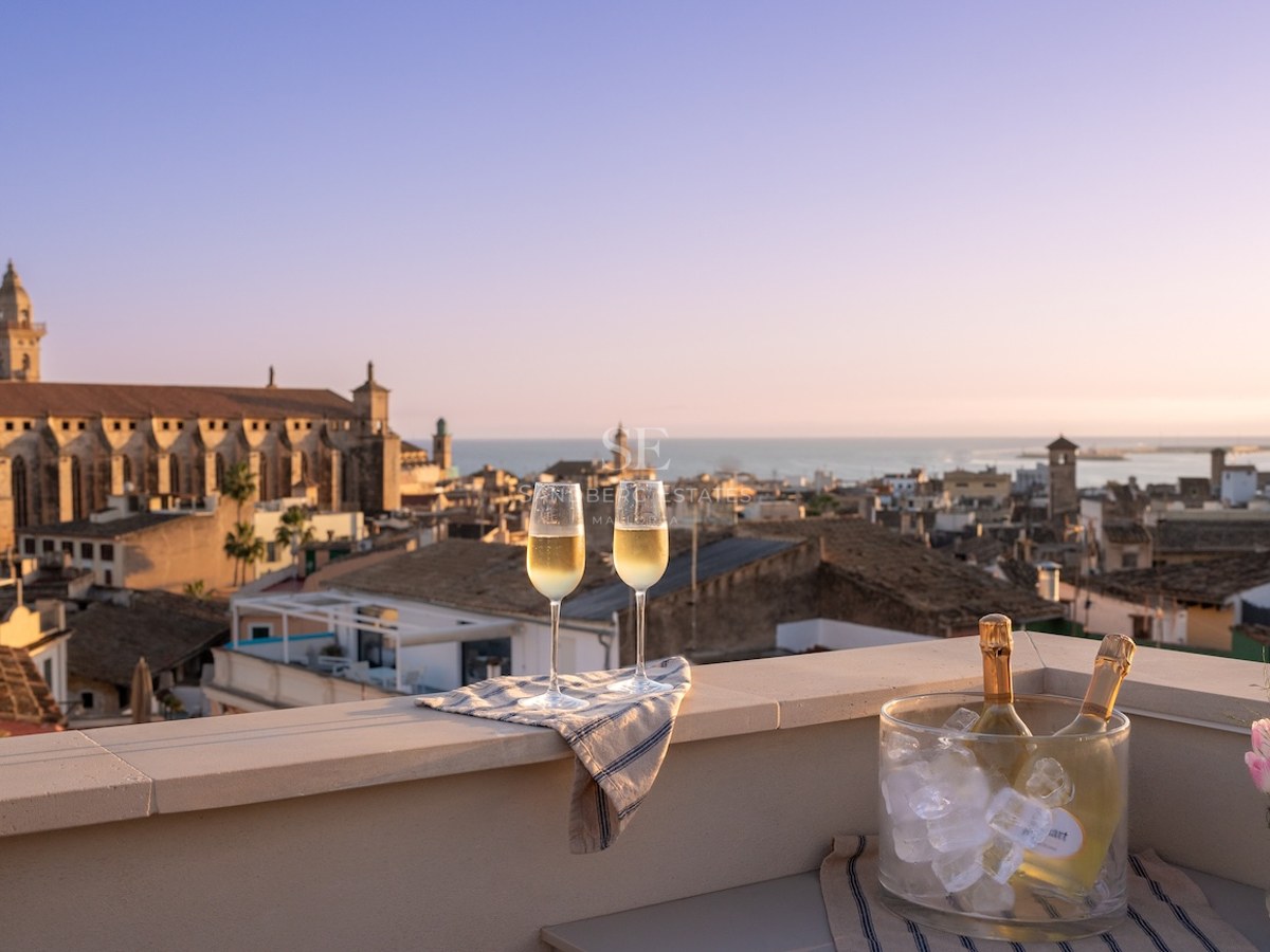 Dos copas de champán y una cubitera en una azotea con vistas a una ciudad costera histórica al atardecer.