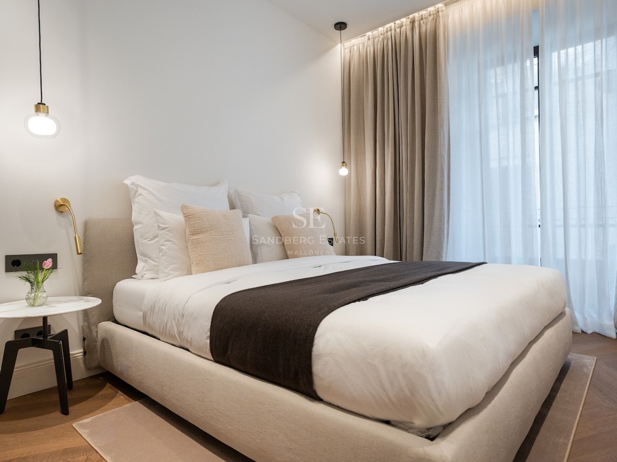 Dormitorio principal moderno con cama beige, mesita de mármol, suelo de parqué y cortinas de techo a suelo.