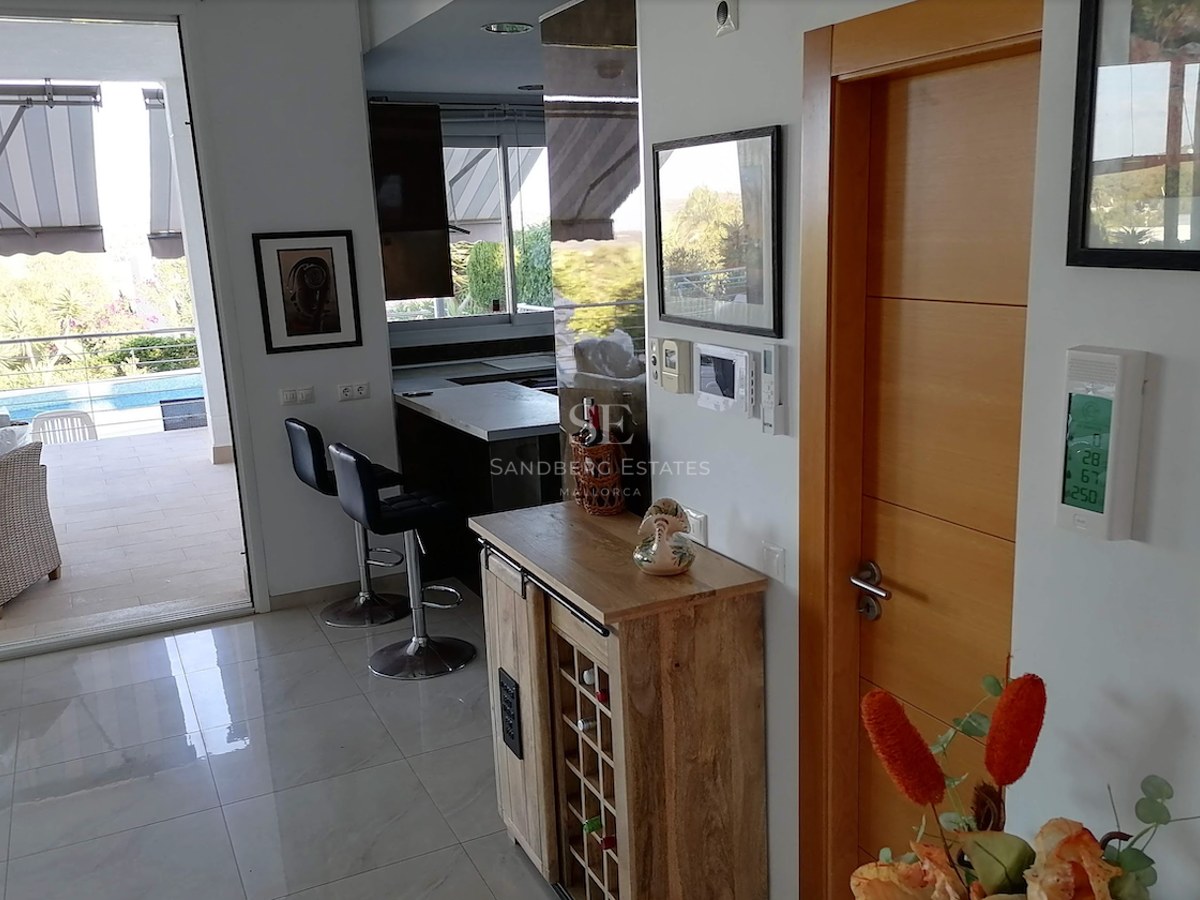 Interior view showing a modern living area with wine cabinet, leading to a sun-drenched terrace and swimming pool.