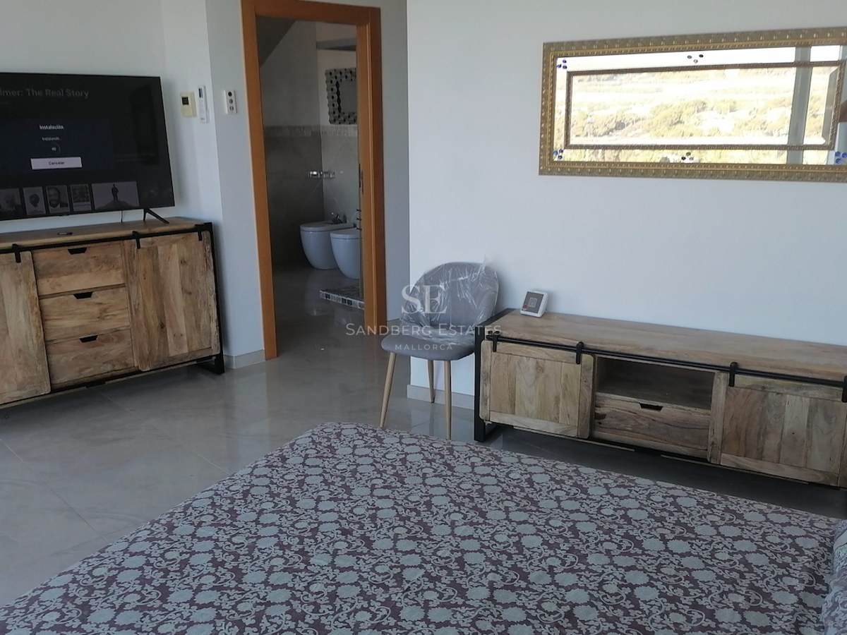 Modern bedroom featuring rustic wood media consoles, a large TV, and a view into a private en-suite bathroom.
