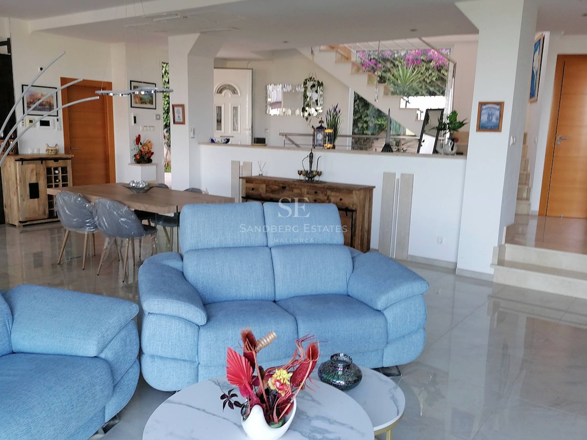 A spacious living room with blue sofas, polished marble floors, and an integrated dining area in a bright modern villa.