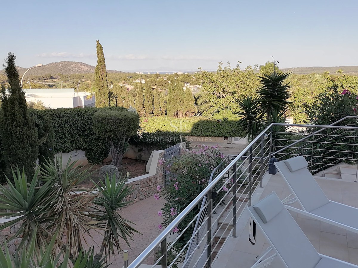 A sun-drenched terrace with modern loungers and stainless steel railings overlooking a lush Mediterranean garden and distant sea.
