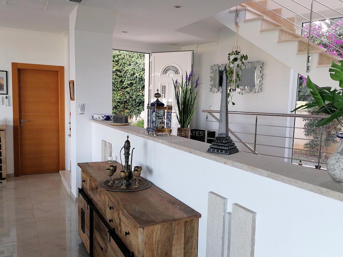 Spacious villa entrance featuring polished marble floors, a wooden sideboard, and an open staircase with steel railings.