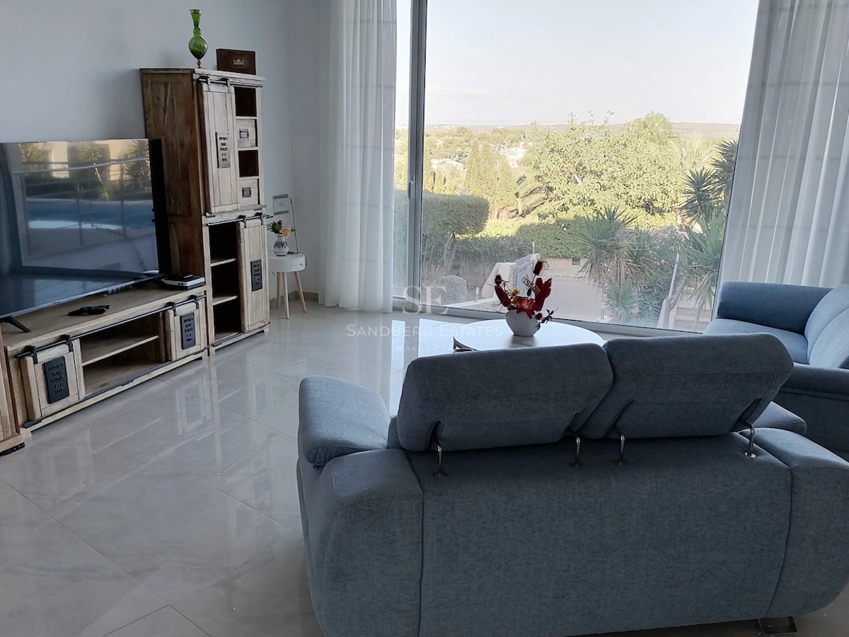 Modern living room featuring grey fabric sofas, polished floor tiles, and a large window overlooking lush greenery.