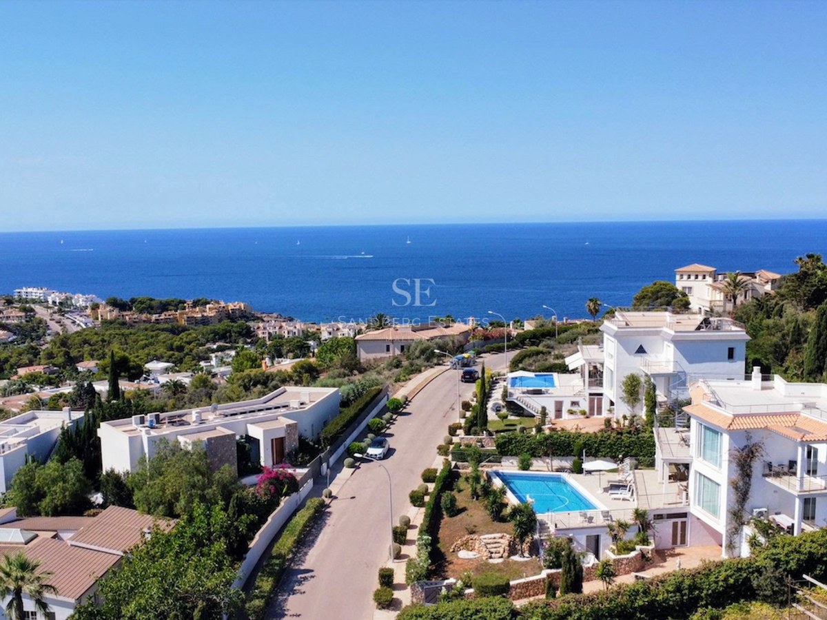 Aerial view of luxury white villas with swimming pools overlooking the deep blue Mediterranean Sea under a clear sky.