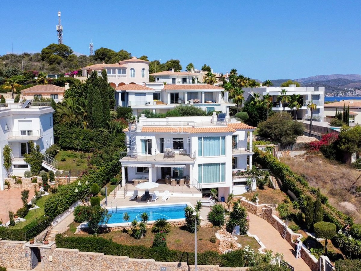 Aerial shot of a white multi-level villa featuring a rectangular turquoise pool, stone walls, and manicured gardens.