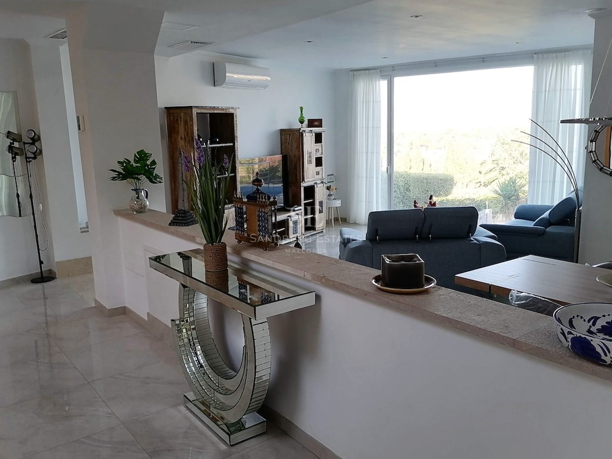 Modern living room featuring marble floors, blue seating, and a large window overlooking lush greenery.